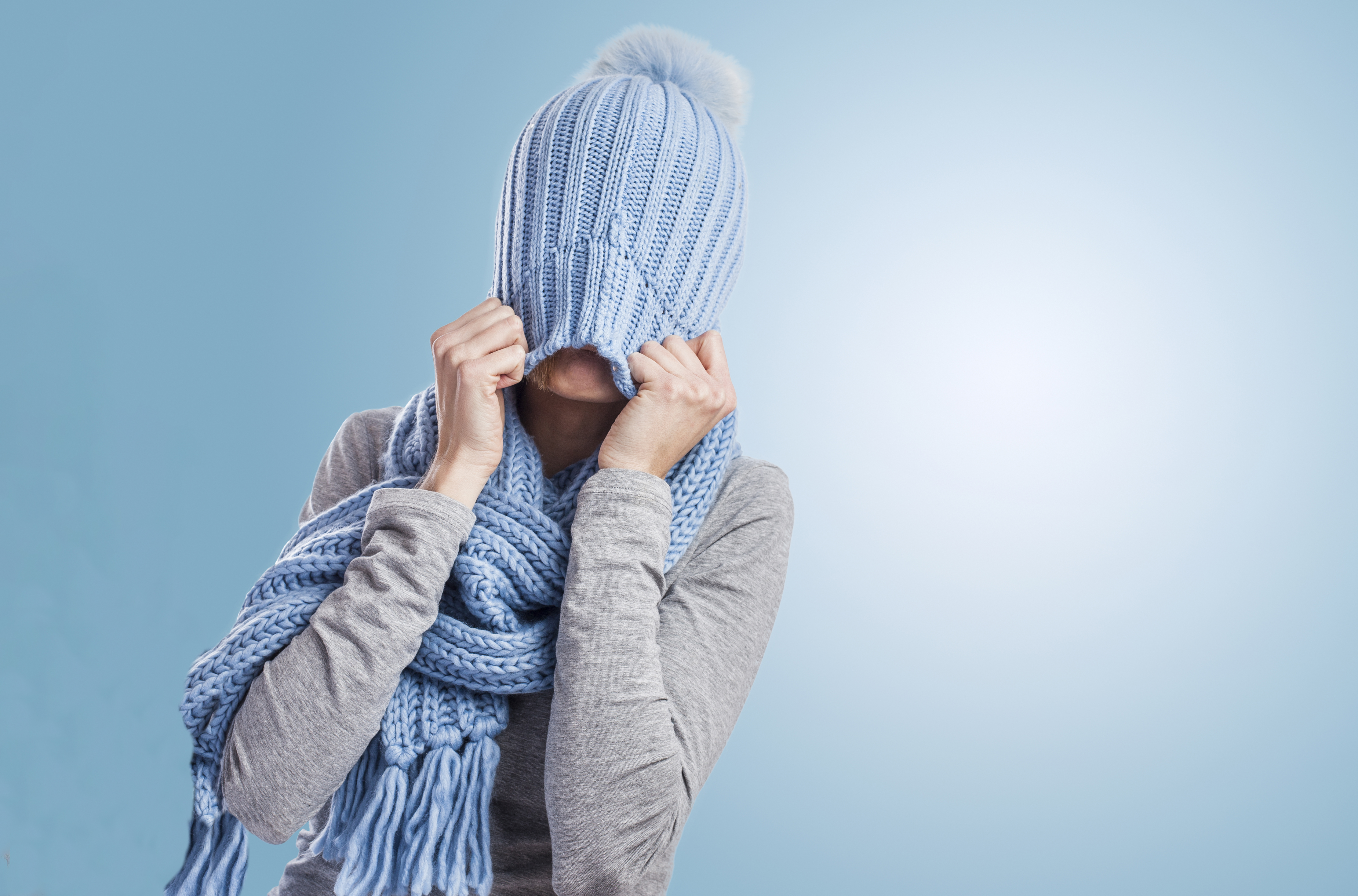 Persona agarrando el gorro de lana que tiene en la cabeza con las manos cubriendo su cara