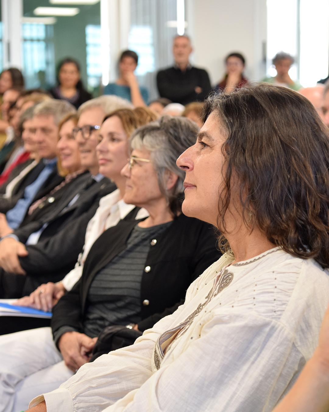 En primer plano de perfil se encuentra la nueva decana electa Alejandra dominguez, de fondo se ven a la decana saliente, vicedecana entrante liliana cordoba, el rector Jhon Boreto y más autoridades, todas de perfil mirando al escenario
