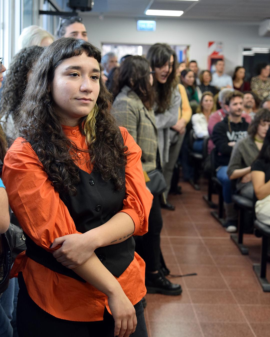 en primer plano una persona mirando al escenario, de fonde hay multitud de personas
