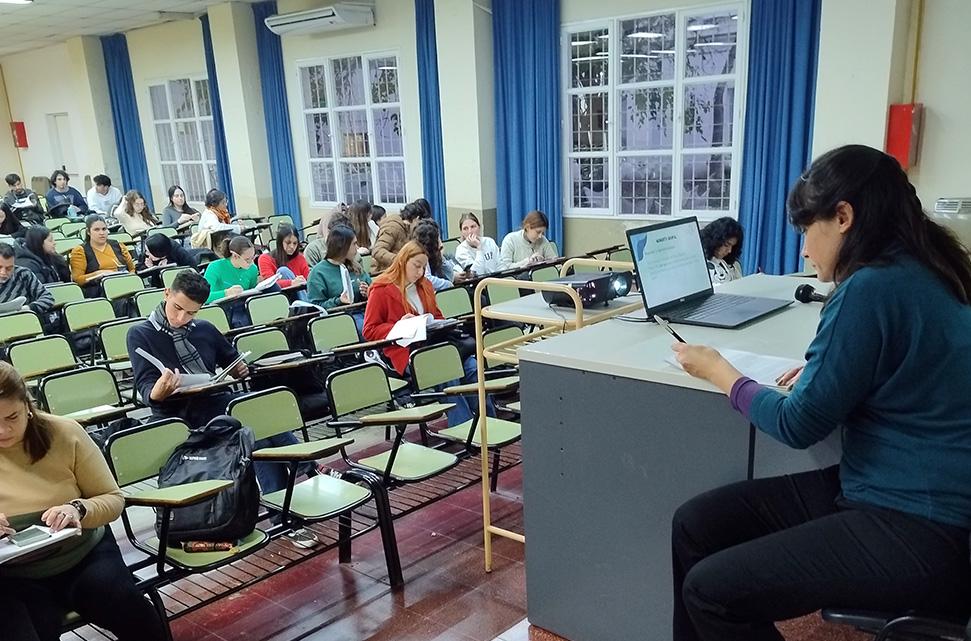 docente-sentada-en-un-aula-en-el-escritorio-y-estudiantes-y-docentes-sentados-en-el-aula