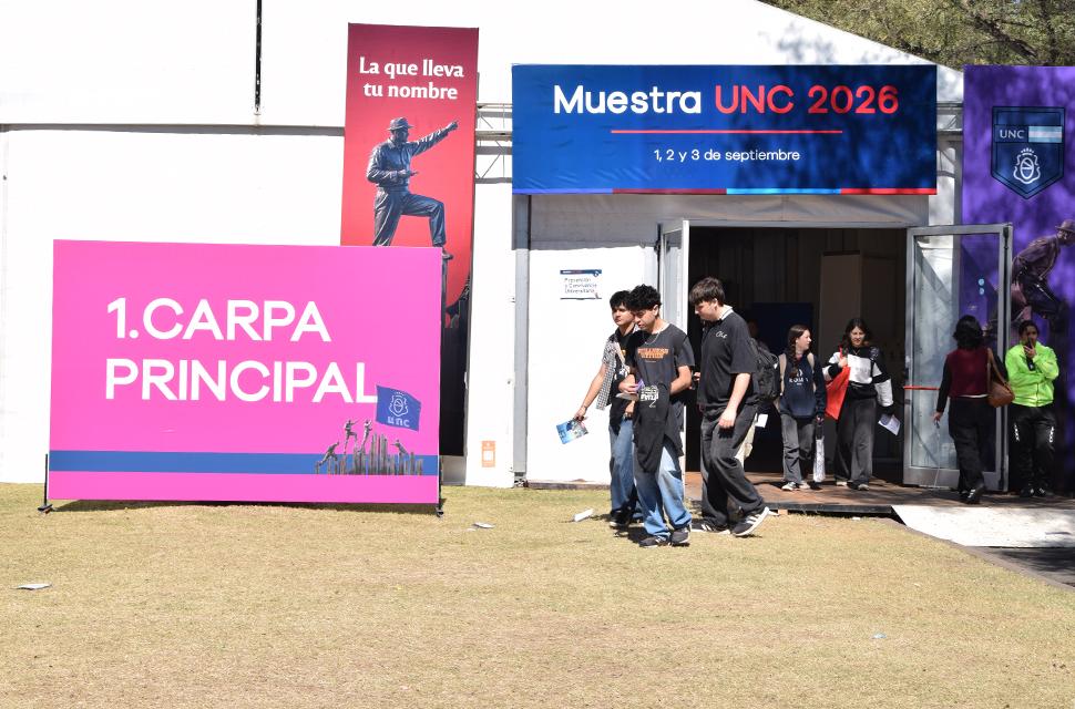 Ingreso a la carpa de la muestra de carreras, estudiantes caminando y cartelería de la muestra