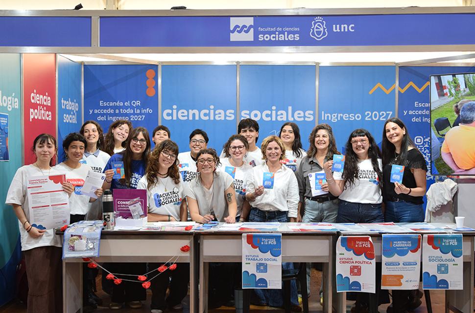 Foto general de voluntaries junto a Decana y vicedecana, y la secretaría de asuntos estuidiantiles en el stand de la Facultad de Cs. Sociales